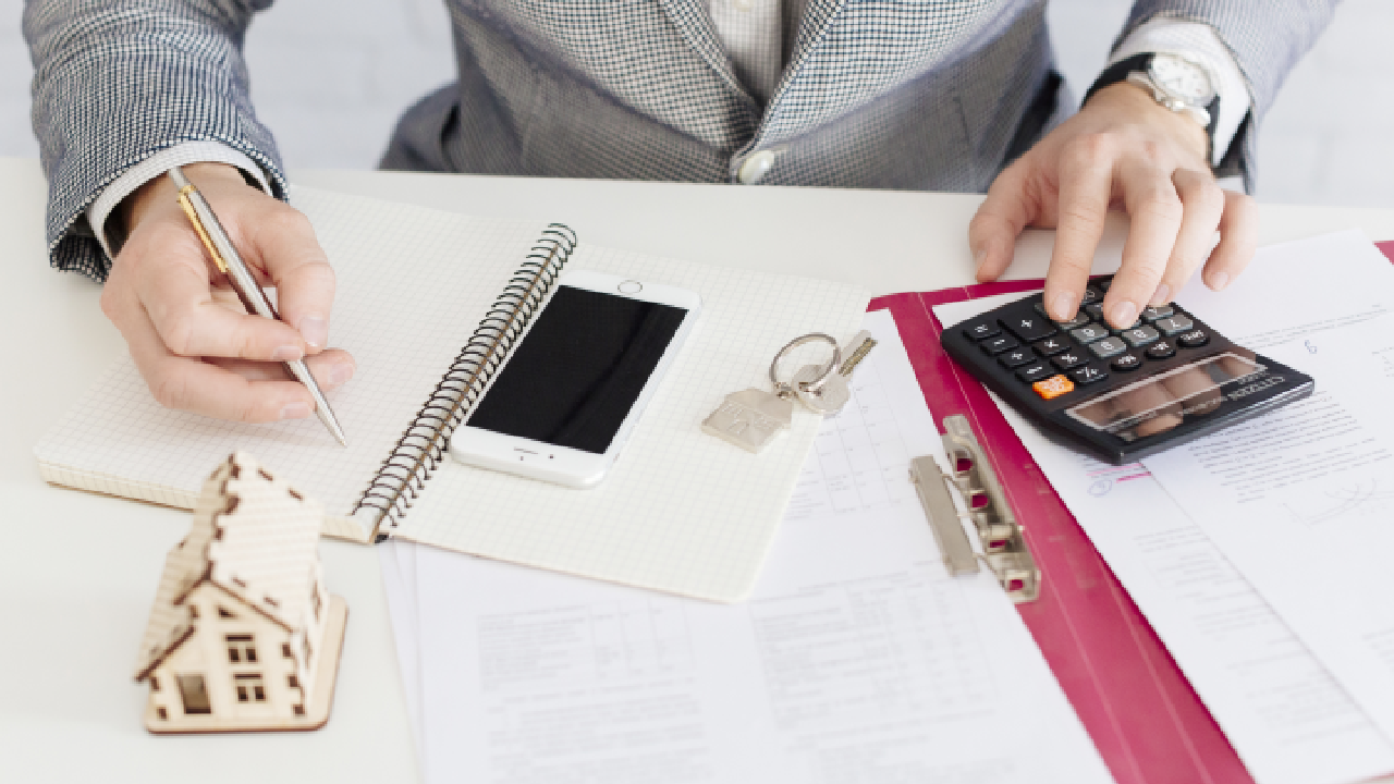 A commercial real estate building with a "For Sale" sign in front, a city skyline in the background, and a calculator alongside financial documents on the ground.